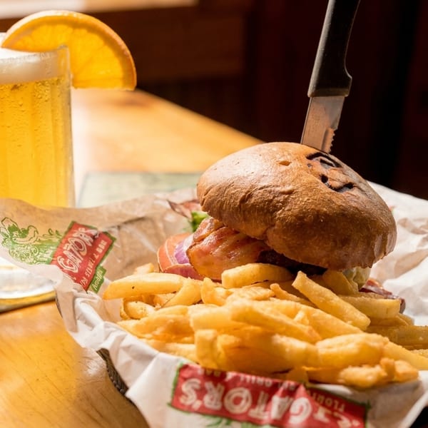 A burger with fries in a basket and a beer mug with an orange slice on a wooden table.