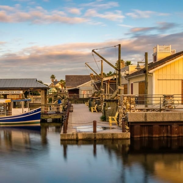 A blue and white boat docked next to a boardwalk with a yellow building under a cloudy sky.