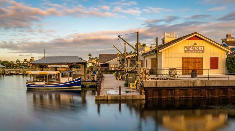 A blue and white boat docked next to a boardwalk with a yellow building under a cloudy sky.