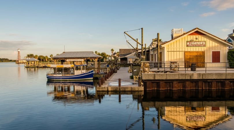 Waterfront view of R.J. Gator's restaurant, a boat, and a distant lighthouse under a clear sky.