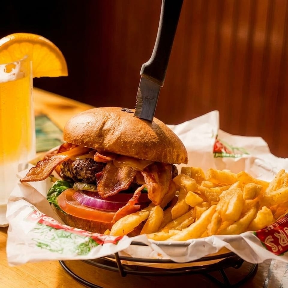 A bacon cheeseburger with fries and a frosty mug of beer with an orange slice.