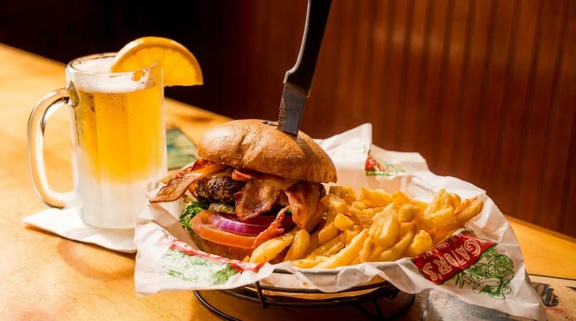 A bacon cheeseburger with fries and a frosty mug of beer with an orange slice.